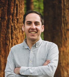 Man stands smiling at the camera with arms crossed